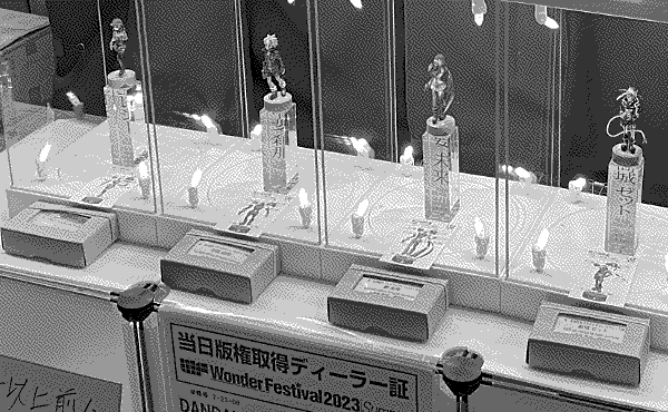 An angled picture showing the boxes for the kits in front of the displays for DANDAN's figures with instructions presented in front.