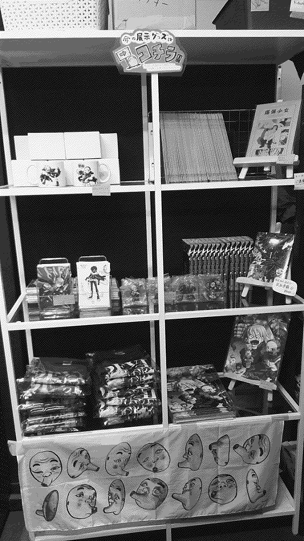 A shelf of prints, posters, pins, mugs, t-shirts, and volumes of Hideaki Fujii's latest manga.